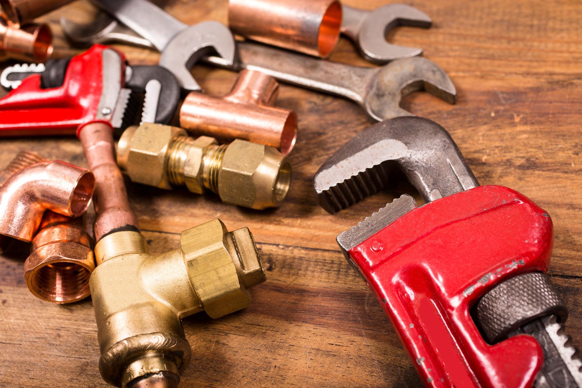 Construction hand tools, plumbing pipes on rustic wooden table.